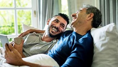 two men looking at each other and smiling in bed